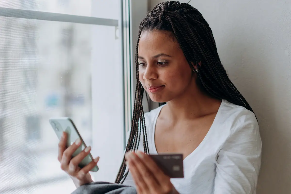 Mujer joven con el celular y su tarjeta junto a una ventana