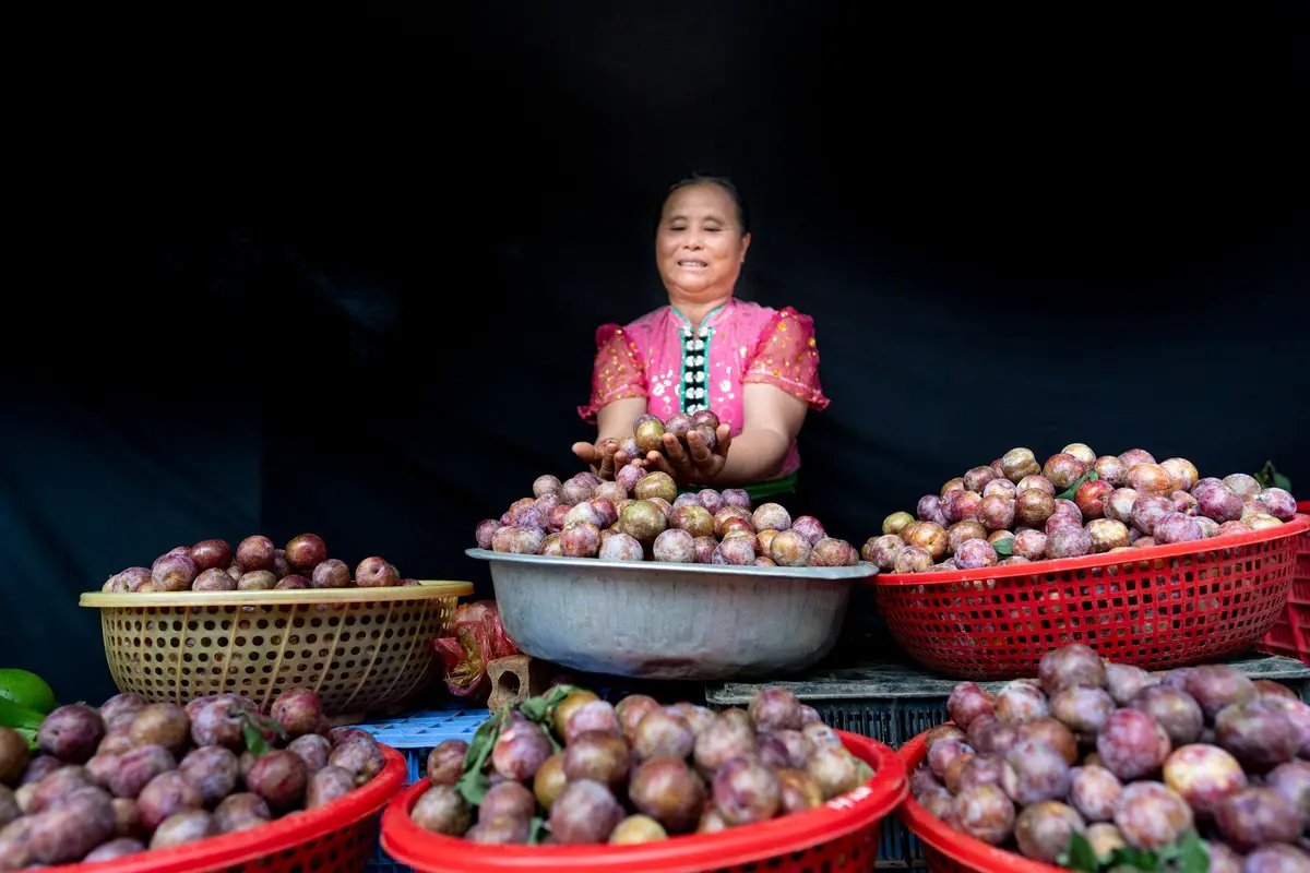 Vendedora sonriente con canastas de ciruelas en su puesto del mercado