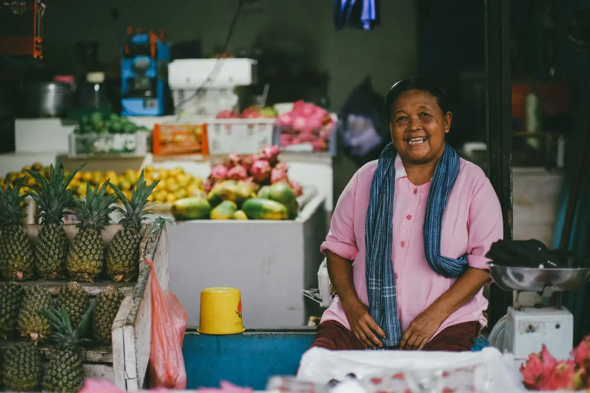 Vendedora sonriente sentada en su puesto de frutas con piñas