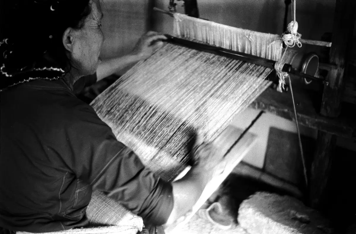 Manos de una mujer tejiendo en un telar, en blanco y negro