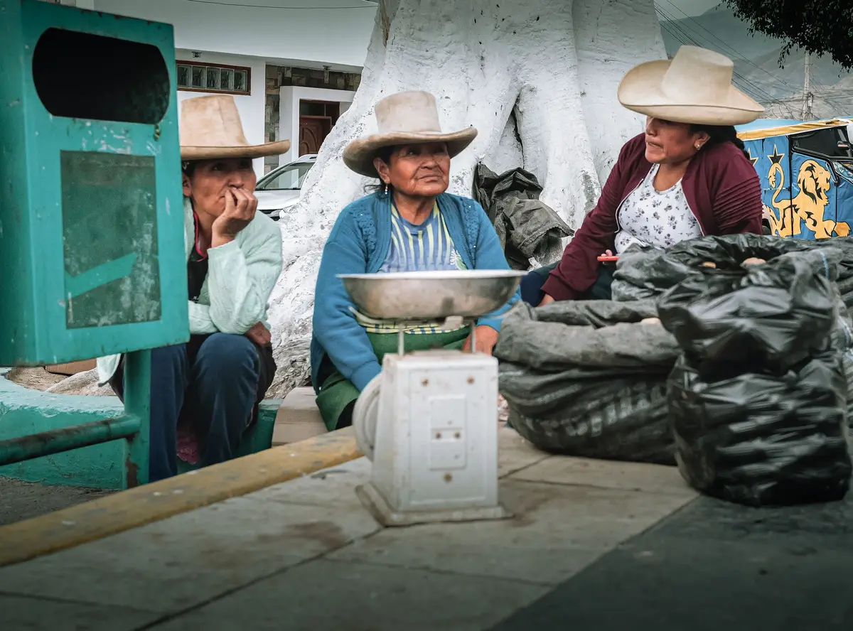 Tres vendedoras con sombrero junto a una balanza y sacos en un mercado de Simbal, Perú