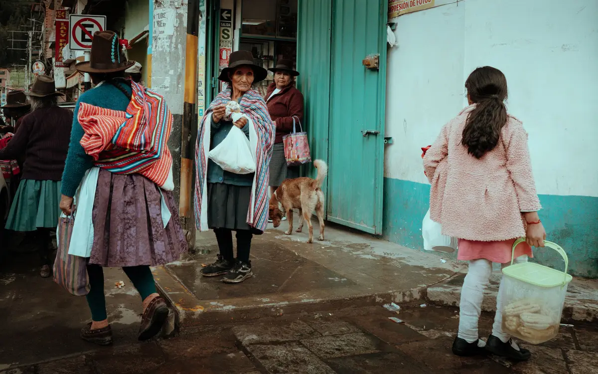 Mujeres con sombrero y manta caminando con sus bolsas por una calle de Huaraz
