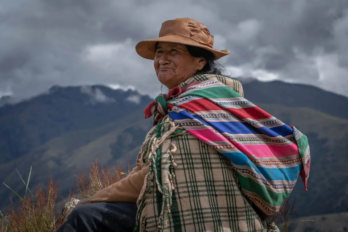 Mujer andina con sombrero y manta de colores frente a los cerros