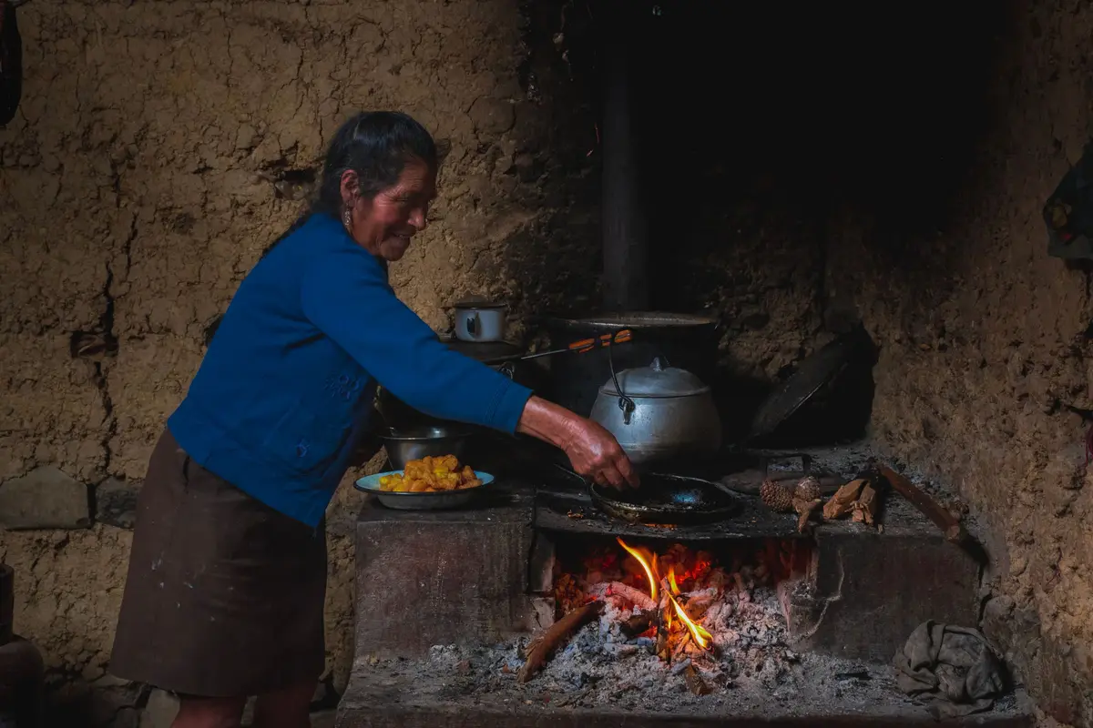 Mujer andina cocinando en su fogón de leña, con un plato de papas doradas a un lado