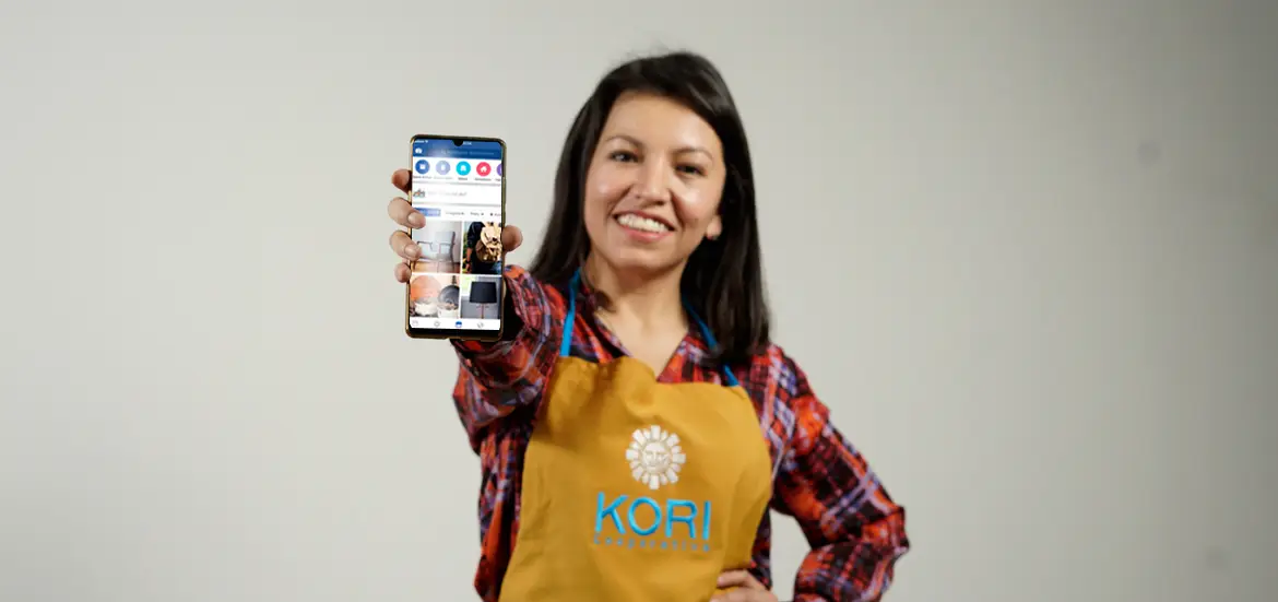 Socia con mandil Kori mostrando el celular, sonriente, sobre fondo gris