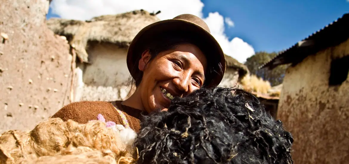 Mujer andina con sombrero sonriendo con un animal